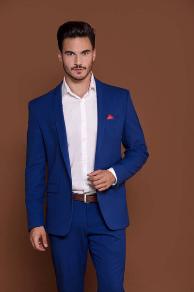 Elegant young man in an expensive fashionable suit posing in the studio, looking at camera.