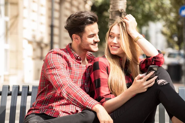微笑情侣在户外约会 年轻快乐的情侣坐着 看着手机 — 图库照片