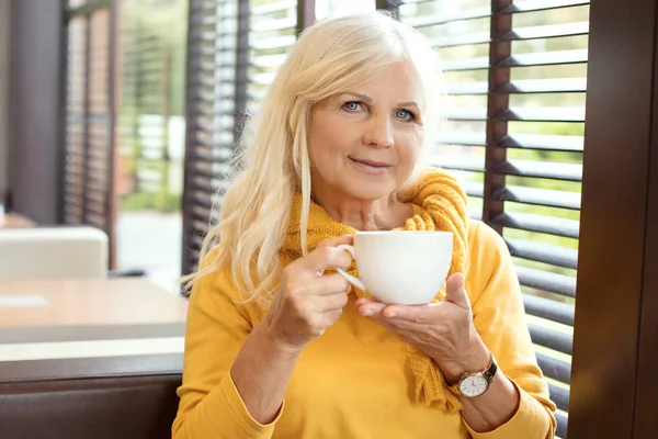 Stylish gorgeous senior woman posing indoors with mug of coffee. Elderly people, modern lifestyle, beauty and fashion concept.