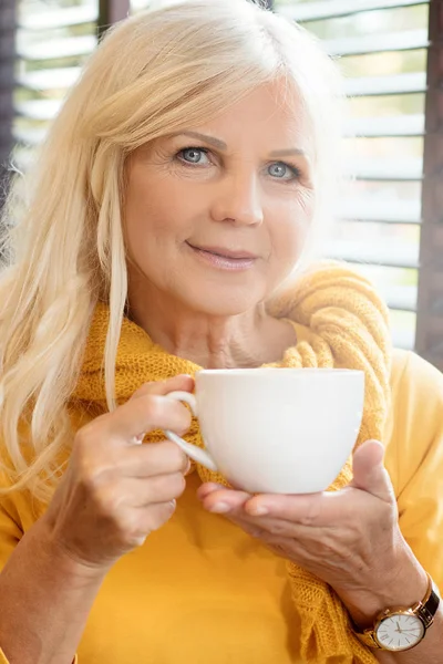 Stylish gorgeous senior woman posing indoors with mug of coffee. Elderly people, modern lifestyle, beauty and fashion concept.