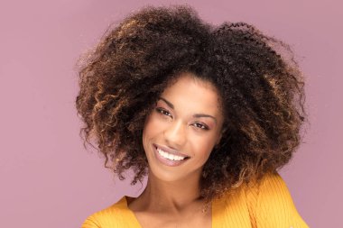 Pembe bir arka plan üzerinde gülümseyerek poz genç afro Amerikalı kadın. İnsan duyguları.