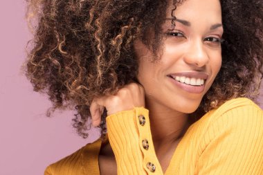 Pembe bir arka plan üzerinde gülümseyerek poz genç afro Amerikalı kadın. İnsan duyguları.