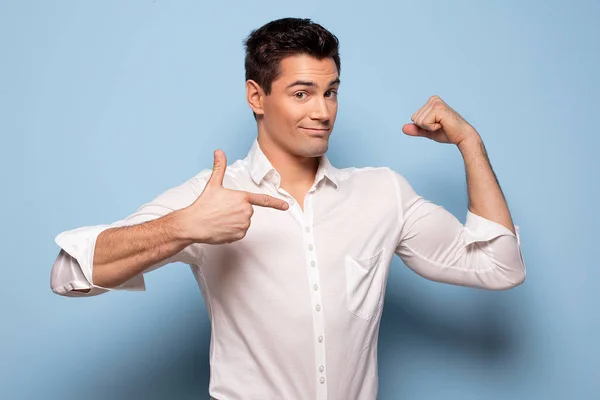 Sonriente Hombre Guapo Apuntando Bíceps Posando Sobre Fondo Azul Pastel —  Fotos de Stock