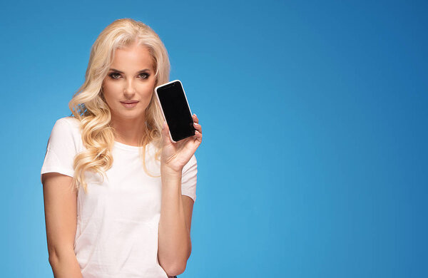 Блондинка, позирующая с мобильным телефоном на фоне синей пастельной студии
.