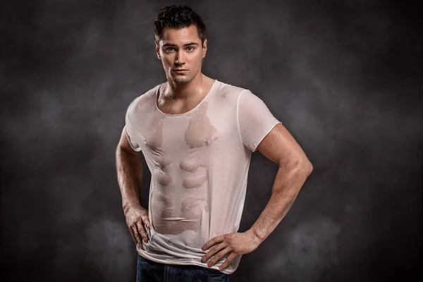 Handsome muscular man posing in wet shirt, looking at camera.