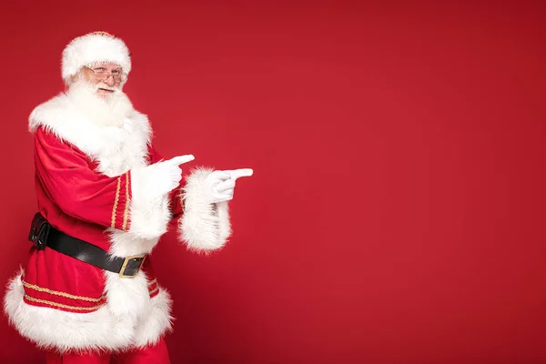 Real Santa Claus pekar på röd studio bakgrund. — Stockfoto