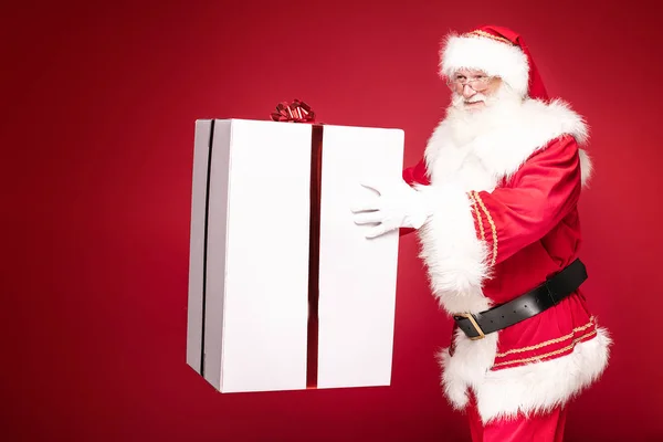 Справжній Санта Клаус усміхається, тримає велику коробку з подарунками.. — стокове фото