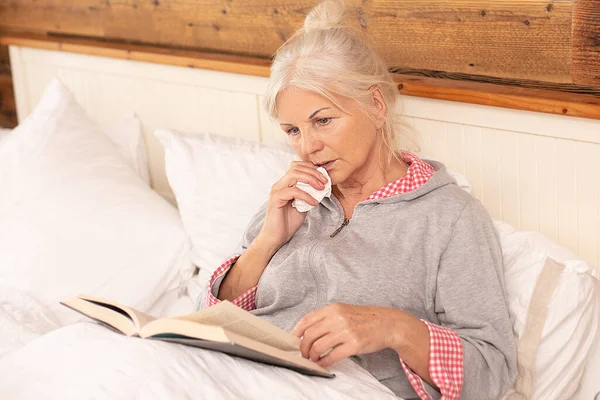 Caucasian senior women relax at home, reading book while lying on bed in bedroom at home .