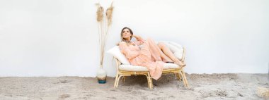 Yaz tatili rahatlama konsepti. Çekici sarışın bir kadın kumlu bir tropikal sahilde bir kanepede oturuyor..