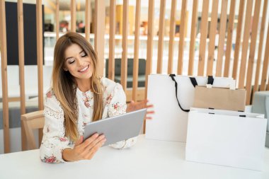 Yüzünde mutlu bir ifade olan çekici bir kız tabletten online alışveriş yapıyor. Mevsimlik satış zamanı.