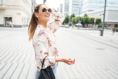 Şık güneş gözlüğü takan genç ve güzel bir kadın mutlu gülümsüyor..