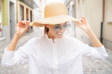 Yazlık şapkalı ve güneş gözlüklü güzel bir kadın mutlu gülümsüyor..