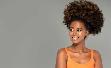 Güzel Afrikalı kadın gülüyor. Kıvırcık saçlı, gri stüdyo arka planında poz veren güzel Afro-Amerikalı kız..