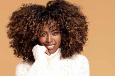 Saçı Afro saçlı, bej renkli stüdyo arka planında rahat bir süveter giyen mutlu, Afrikalı bir kız..