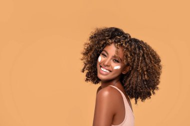 Yüzünde nemlendirici olan genç bir afro kadın. Güzel Afrikalı kız yanağına krem sürüyor. Mükemmel ve sağlıklı ciltli güzel kız..
