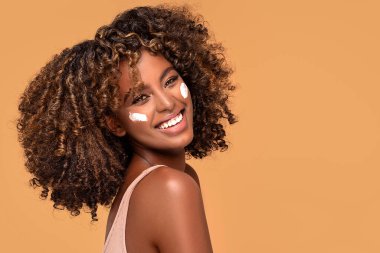 Yüzünde nemlendirici olan genç bir afro kadın. Güzel Afrikalı kız yanağına krem sürüyor. Mükemmel ve sağlıklı ciltli güzel kız..