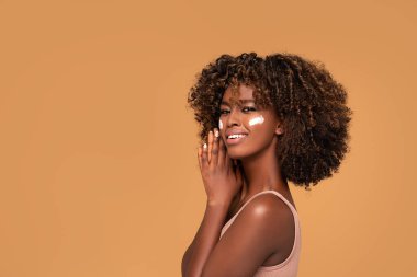 Yüzünde nemlendirici olan genç bir afro kadın. Mükemmel ve sağlıklı ciltli güzel kız..