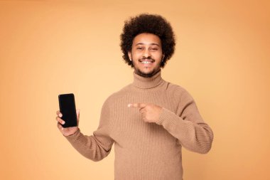 Gülümseyen Afro-Amerikan adam stüdyoda cep telefonunu gösteriyor. Halk yaşam tarzı konsepti.
