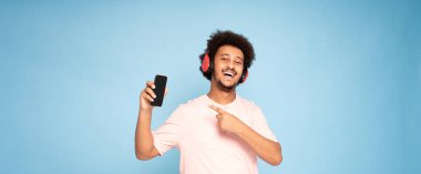 Sıradan tişörtlü neşeli Afrikalı adam elinde cep telefonu, gülümsüyor..