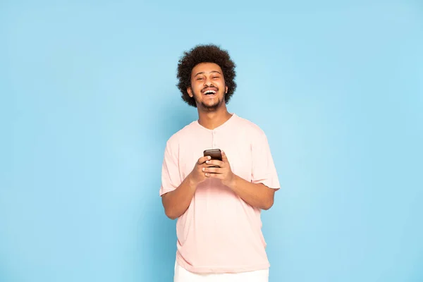 Cheerful young african guy in casual t-shirt holding mobile phone , smiling.