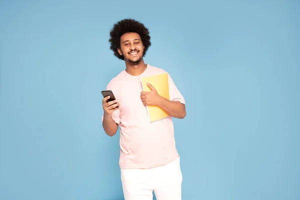 Wesoły Młody Afrykanin Luźnej Koszulce Telefonem Komórkowym Notatnikiem Uśmiechnięty — Zdjęcie stockowe