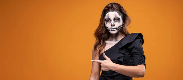 Portrait of a woman with skull makeup over yellow studio background. Halloween costume and make-up.