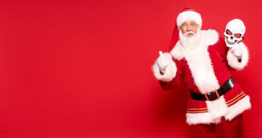 Gerçek Noel Baba 'nın elinde cadılar bayramı kafatası maskesi tutarken çekilmiş komik bir fotoğrafı..