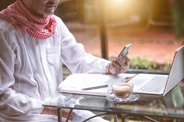 Pakistanlı Müslüman Adam kahve dükkanında dizüstü bilgisayar ve cep telefonuyla çalışıyor.
