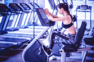 Asya 'lı genç bir kadın bisiklete biniyor. Spor salonunda.