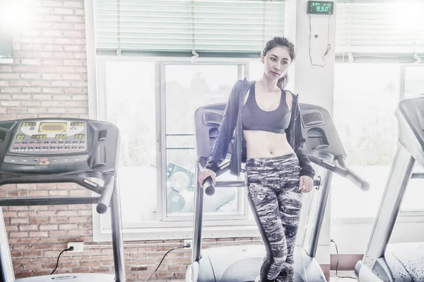 Spor salonundaki koşu bandında koşan Asyalı kadın.