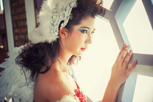 窓の近くに赤いドレスの白い角度の翼を持つ美しい若い女性 — ストック写真