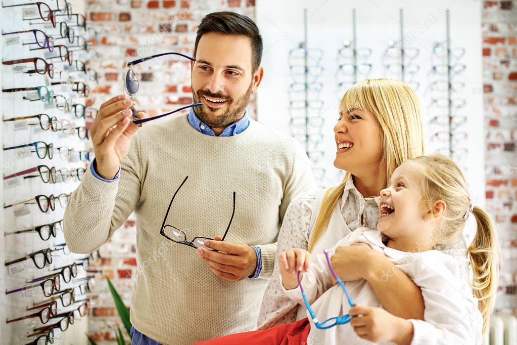 Happy family choosing glasses in optics store. 