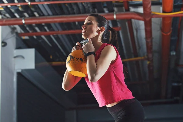 Young athelete woman is training in garage using kettle bell.