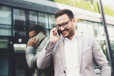 Genç gülümseyen işadamı dışındaki telefon kullanıyor.