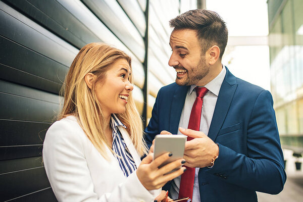 Young business people are relaxing in front of the company building and discussing about new project.