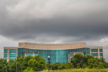 Snellville, Ga / USA - 07 06: 20: Tepesinde kara bulutlar olan ağaçların arasından cam pencereli yüksek bir bina