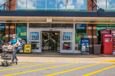 Snellville, Ga / USA - 07: 14: 20: Mavi tişörtlü ve güneş gözlüklü kadın Kroger mağazasından yüz maskesi takarak çıkıyor ve covid-19 salgını sırasında alışveriş arabasını itiyor.