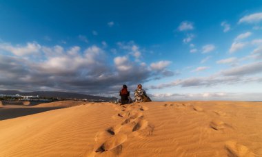 Genç bir çift manzaranın tadını çıkarmak için kumulun tepesinde oturuyor. Maspalomas Kumulları (Gran Canaria). Seyahat fotoğrafçılığı. manzara