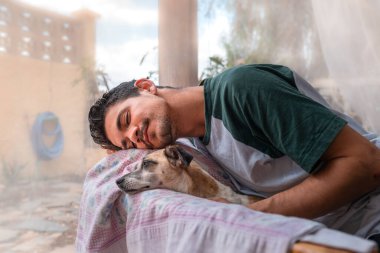 Genç bir adam, köpeği ile birlikte bahçedeki koltukta, sivrisinek ağının altında uyuyor.