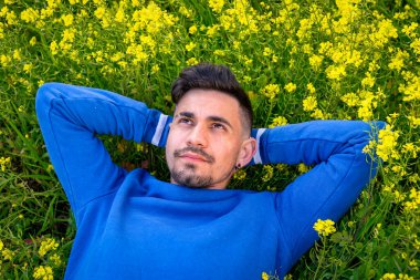 Genç adam sarı çiçeklerle dolu bir tarlada yatıyor. Doğanın tadını çıkarıyor. Kapat.