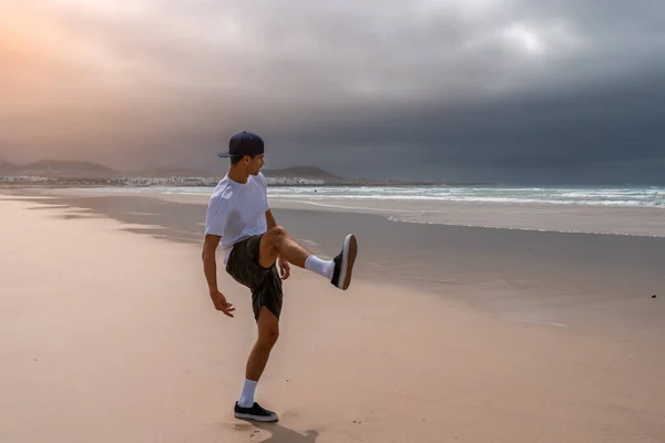 Young man plays throwing stones into the sea on Famara beach at sunset. Teguise Lanzarote Canary Islands