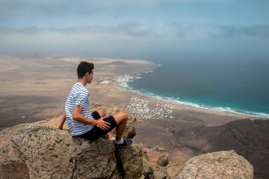 Uçurumun tepesinde oturan genç adam Famara Sahili 'ni seyrediyor. Lanzarote (Kanarya Adaları)