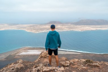 Lanzarote adasındaki bir uçurumun tepesindeki genç gezgin arka plandaki Graciosa Adası 'na bakar. Lanzarote. Kanarya Adaları