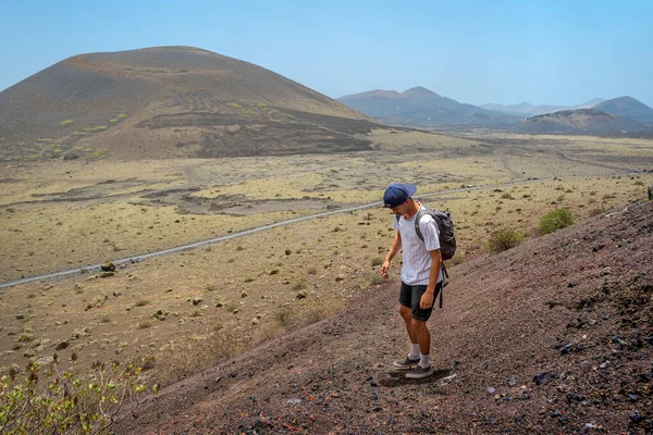 Genç adam Montaa Colorada yanardağının tepesine tırmanışın ortasında dinlenmek için duruyor. Timanfaya Ulusal Parkı. Lanzarote. Kanarya Adaları