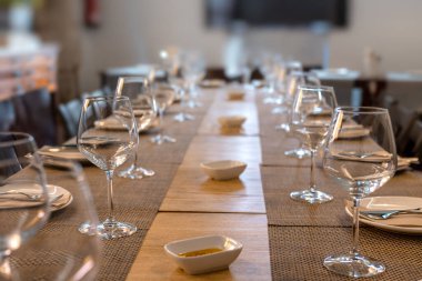 Bardakları, çatal bıçakları ve zeytinyağı olan birçok restoran masası.
