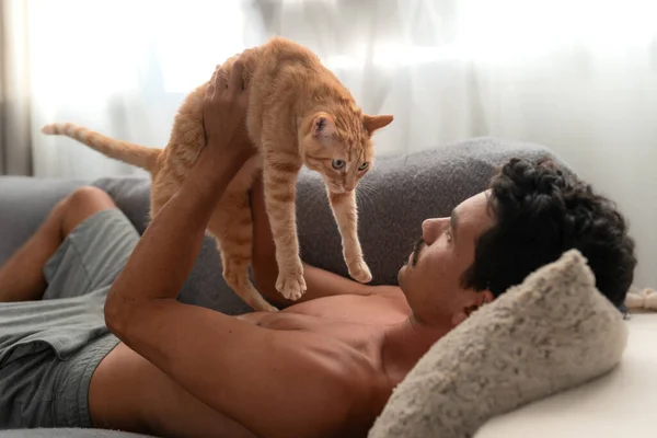 Młody Człowiek Leżący Kanapie Bawi Się Brązowym Kotem Tabby — Zdjęcie stockowe