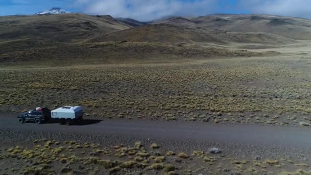 空中无人机场景的面包车和拖车 旅宿汽车在草原 巴塔哥尼亚阿根廷骑在一个砾石偏僻的道路 Tromen 火山的背景 国家公园 相机移动左跟踪车 — 图库视频影像