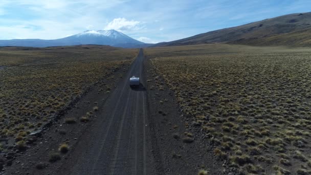 空中无人机面包车和拖车 旅宿汽车在草原 巴塔哥尼亚阿根廷骑在碎石孤独的道路上 怀勒山在背景 Tromen 火山国家公园 摄像头移动前跟踪车 — 图库视频影像