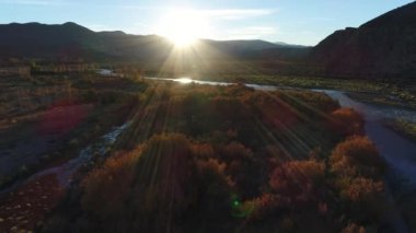 Rüzgarlı bir gün, arka ışık parlama ile gün batımı, altın saatin nehirde barrancas hava dron sahne. Nehir Neuquen - Mendoza, Arjantin böler. Kamera hareket iletir. Ağaçlarda sonbahar renkleri