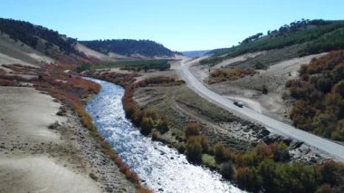 Litran nehir ve çakıl yol hava dron sahne. Renkli Sonbahar bitki örtüsü, riverbend. Yol seyahat römork ile van. Kamera nehir ve yol Villa Pehuenia - Moquehue arasında yayılıyor. Patagonya Arjantin.